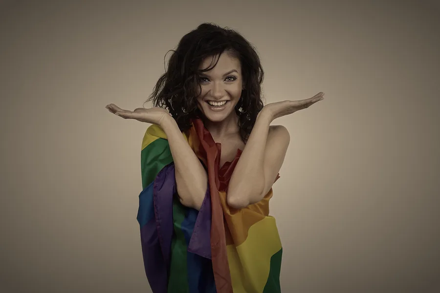 Persona sonriente con la bandera del orgullo LGTBI sobre los hombros